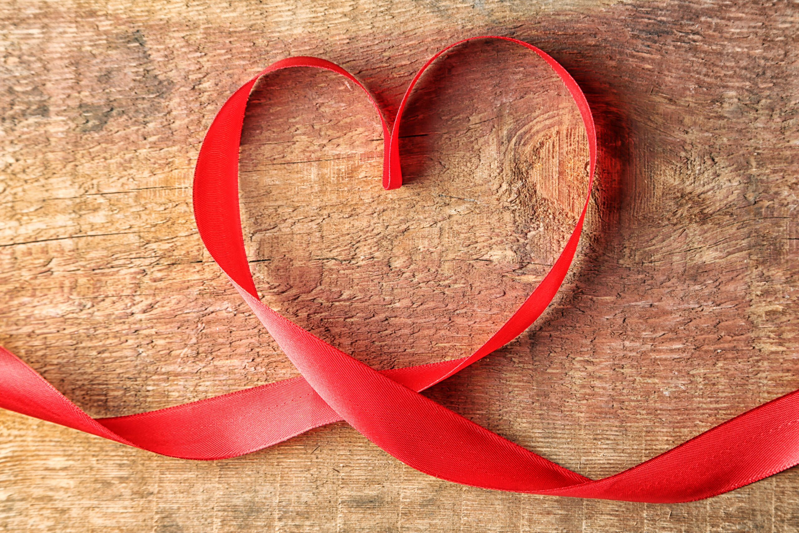 HIV red ribbon in shape of heart against wood background.