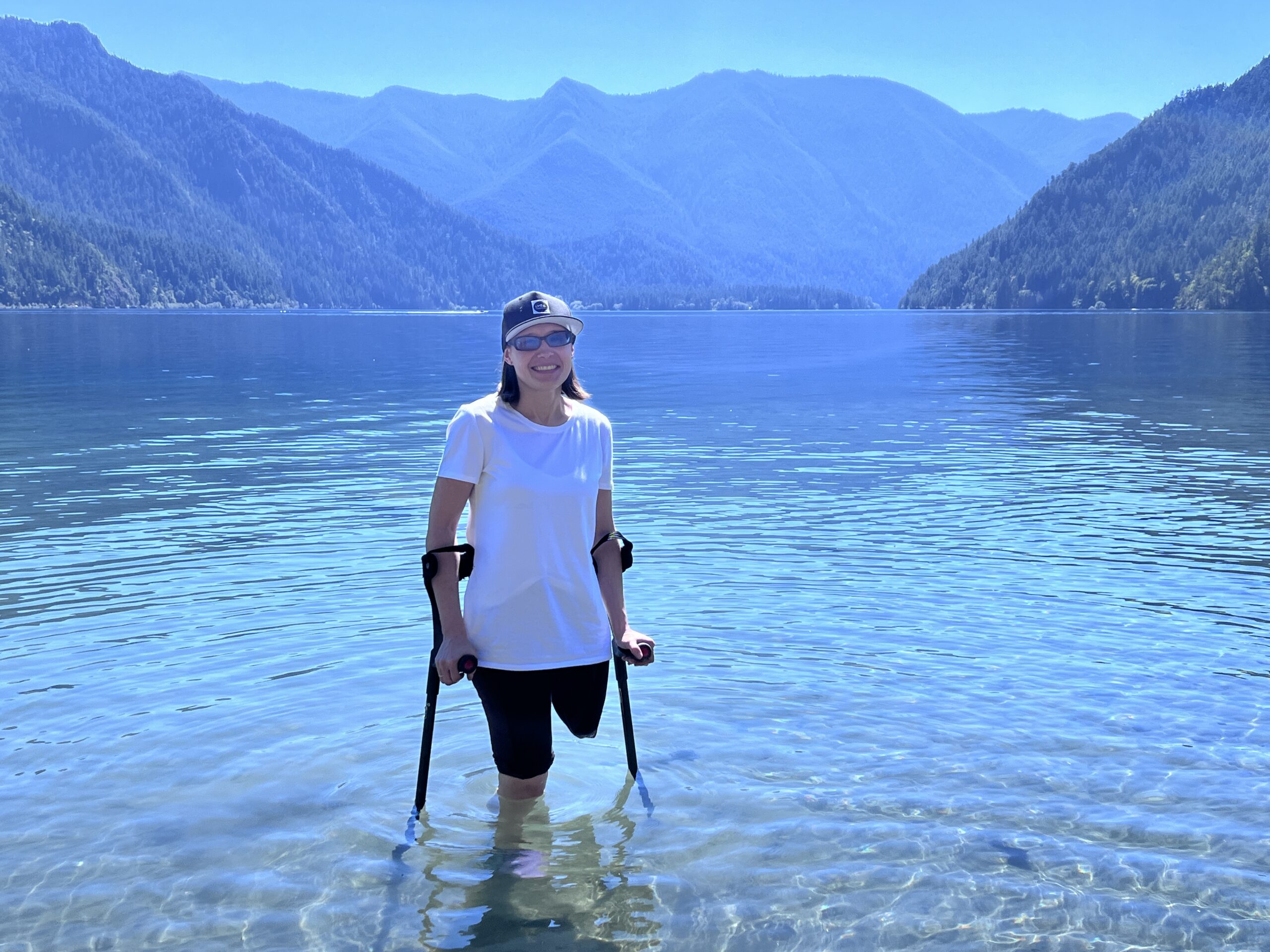 Alfiya Battalova, researcher, is standing in water at Olympic National Park. She is wearing a white shirt, dark shorts and a cap.