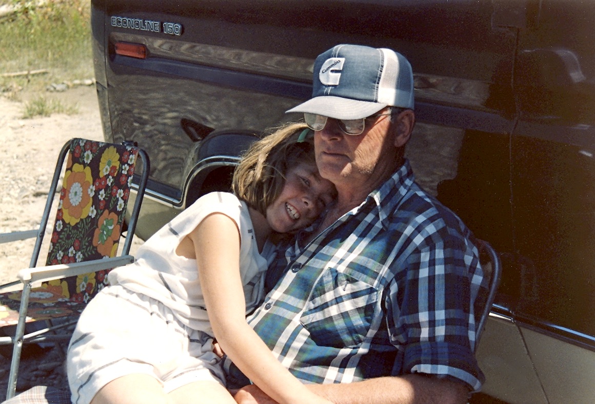 Photo of Heather (aged 9) sitting on their grandpa's lap. He looks grumpy but was loving the cuddle. Heather and Colleen called him Grumps.