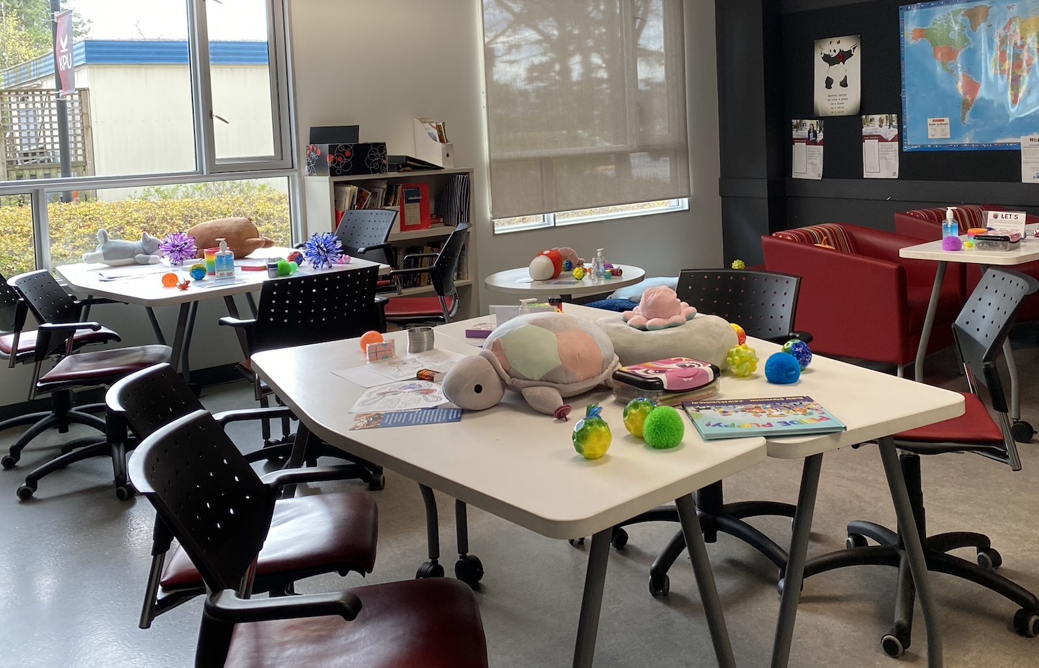 Classroom with tables covered in stuffies, stim toys, books, and colouring sheets.