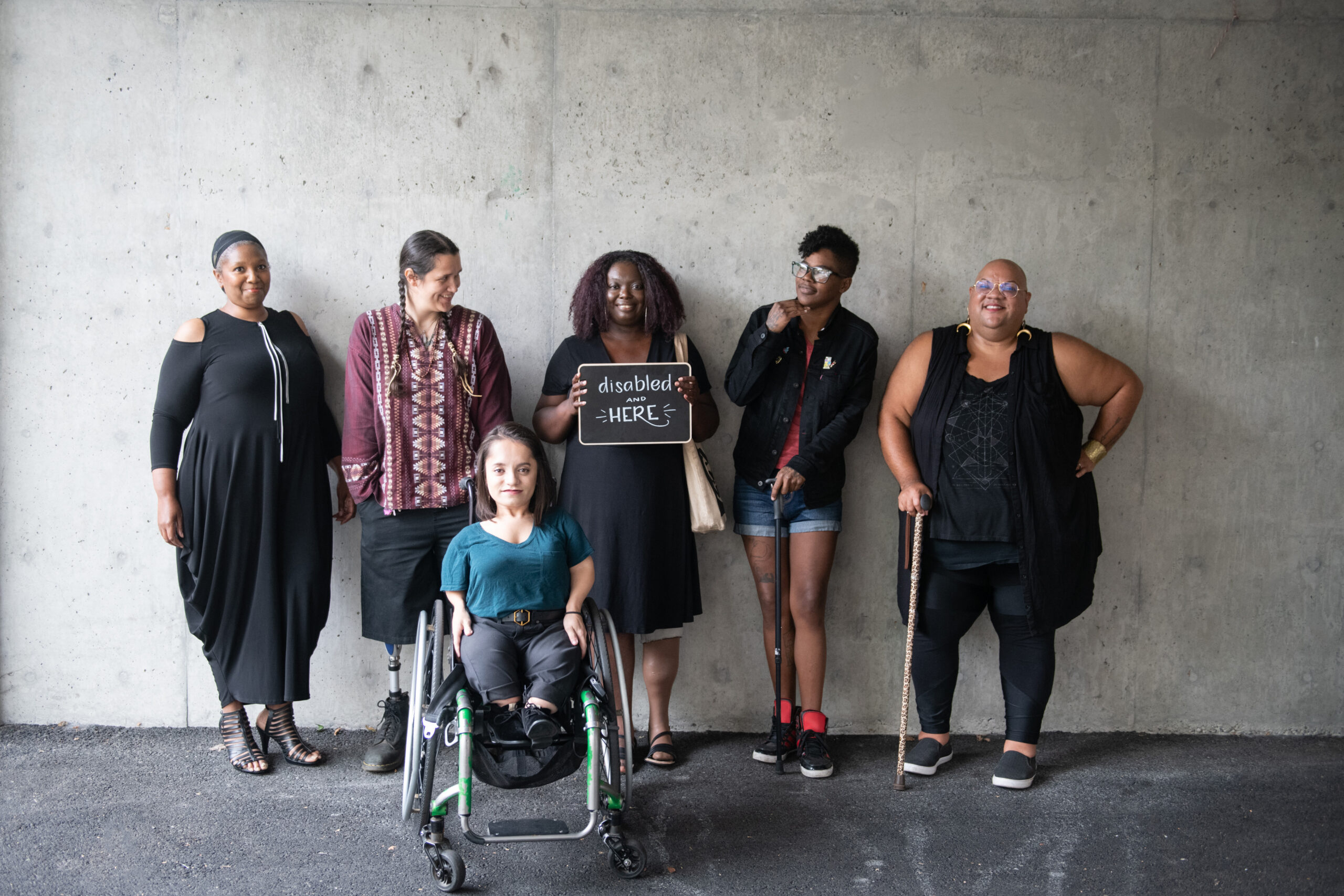 6 disabled people standing in front of wall.