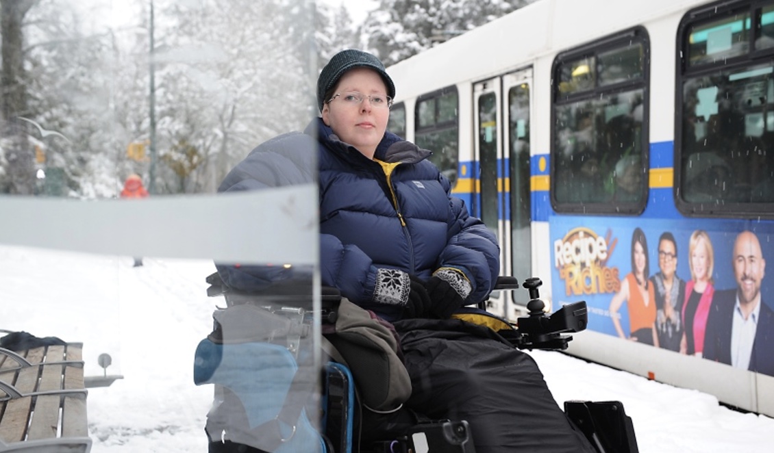 Heather McCain in power chair waiting at bus stop.