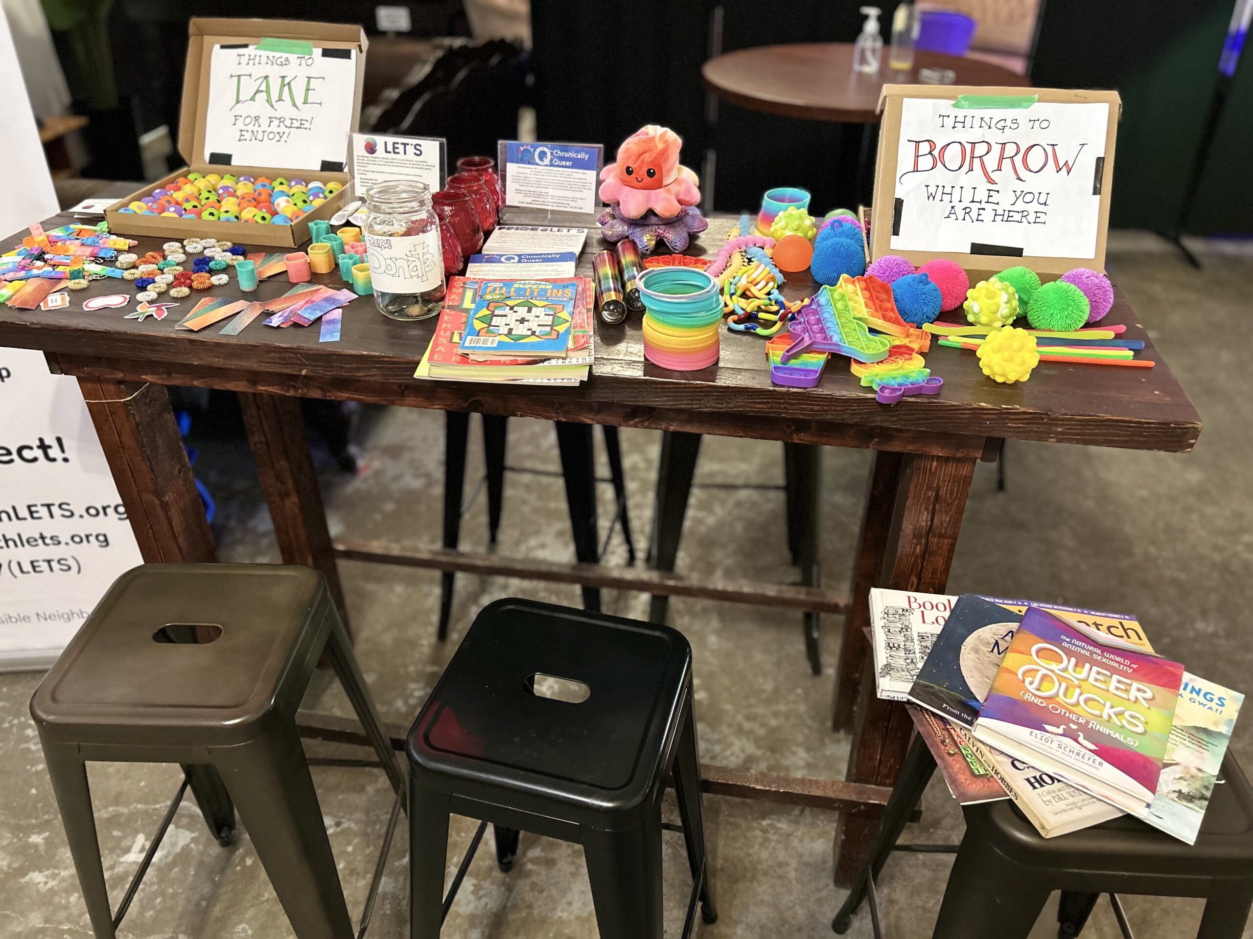 A table with fidget/stim (stimulation) items. Some items are for visitors to use in the space only and others are for them to keep.