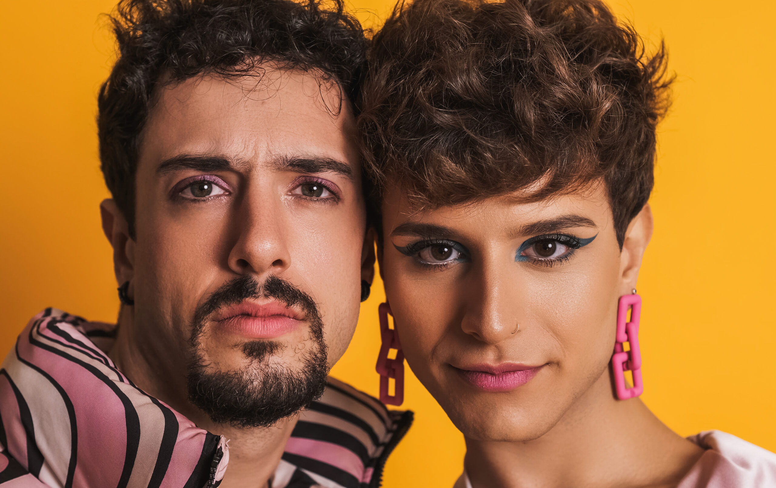 2 people staring directly at the viewer. They are in front of an orange background.
